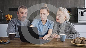 A happy family, a young woman teaching her grandparents how to use a laptop. Senior man and woman, pensioners