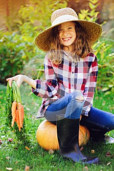 Happy farmer child girl picking fresh home growth carrot harvest from own garden