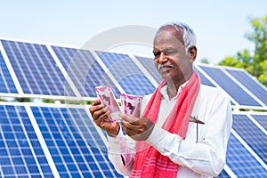 Happy farmer counting money or currency notes in front of solar panel at farmland - concept of loan approval, bank