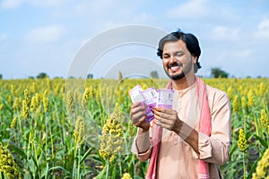 Happy farmer couting money or currency at agricultural farmland - concept of profit or earnings, banking or financial