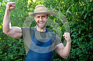 Happy farmer man in farmers hat and apron make winning gesture in garden aoutdoors