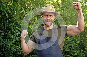 Happy farmer man in farmers hat and apron make winning gesture in garden aoutdoors