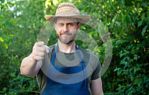 Happy farmer man in farmers hat and apron pointing finger forward natural outdoors