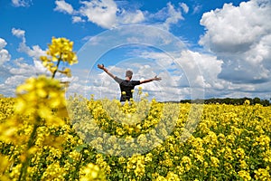 A happy farmer stands in a rapeseed field with his hands up