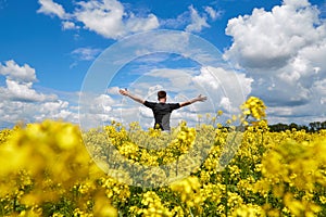 A happy farmer stands in a rapeseed field with his hands up