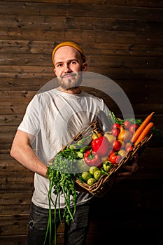 a happy farmer in a white T-shirt and hat holds a basket of fresh fruits and vegetables