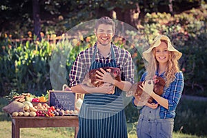 Happy farmers standing at their stall and holding chicken