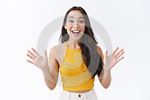 Happy, fascinated good-looking stylish modern asian woman in yellow top, raise hands sideways and smiling as emotionally