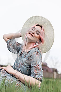 Happy fashion model lovely young woman with smile with colored hair in elegant blue dress with floral print in hat rests on green