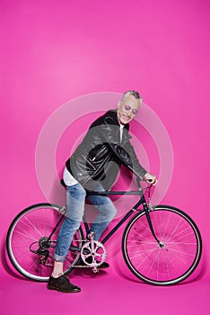 Happy fashionable senior man wearing leather jacket, sunglesses and riding bicycle