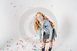 Happy fashionably dressed curly hair tween girl in in denim jacket and black tutu skirt and rough boots on white background with