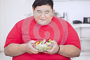 Happy fat man holding salad in the kitchen