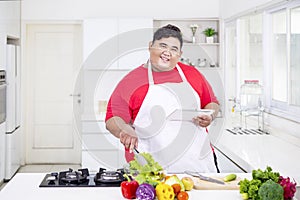 Happy fat man mixing salad while holding a tablet