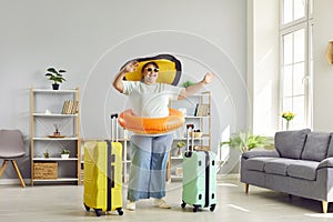 Happy fat woman in hat and sunglasses getting ready for holiday trip standing with suitcase at home