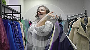 Happy fat woman holding armful of clothes in plus size store.