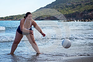 Happy fat woman playing ball on the beach