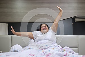 Happy fat woman stretching hands after wake up