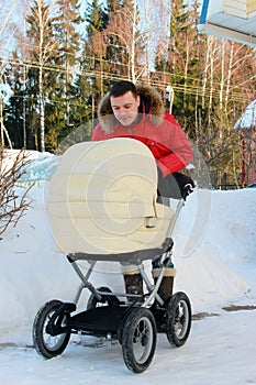 happy father admires baby sleeping in perambulator next to him in backyard with snowdrifts in background on winter sunny day