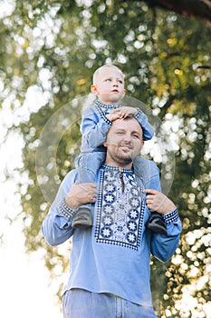 Happy father carries his son on his shoulders during walk on park