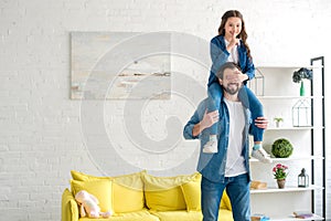 happy father carrying smiling daughter on neck and having fun together at home photo