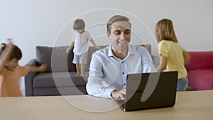 Happy father chatting on laptop and kids playing behind him