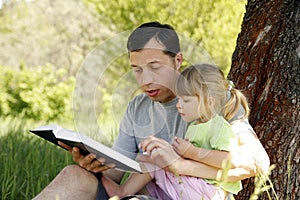 Happy father with a child reading a book on the nature of the Bible