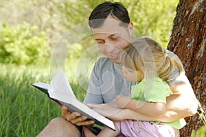 Happy father with a child reading a book on the nature of the Bible