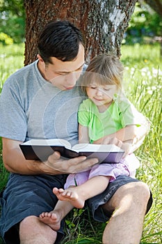 A happy father with a child reading a book on the nature of the Bible