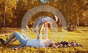 Happy father with child son having fun holding on hands lying on grass, autumn evening sunny family photo