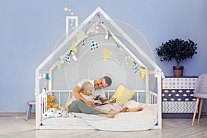 Happy father dad in cute house bed with blonde daughter reading stories at bedtime