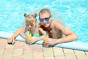 Happy father and daughter with glasses of juice resting in swimming pool