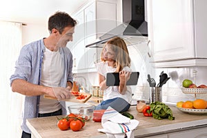 Happy father and daughter looking knowingly cooking with tablet photo