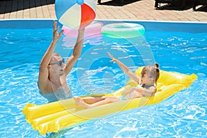 Happy father with daughter playing with ball in swimming pool