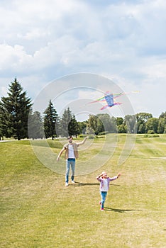 happy father and daughter playing with kite and running on lawn