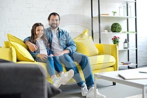 happy father and daughter sitting together on yellow couch and smiling