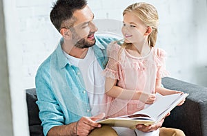 happy father and daughter smiling each other while reading book together photo