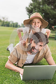 happy father and daughter using laptop and smiling at camera