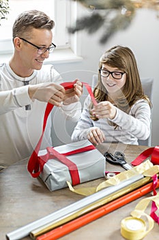 Happy father and daughter wrapping Christmas present at home