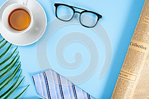 Happy Father Day background concept with blue necktie, glasses, newspaper, leaf and cup of tea on blue background with copy space