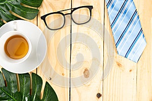 Happy Father Day background concept with blue necktie, leaf, glasses and cup of tea on wooden background with copy space for text