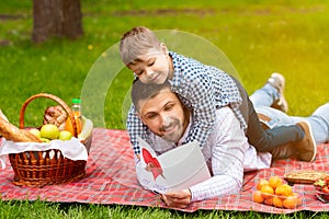 Happy Father Day. Cute child hugging his dad, while he is reading greeting card on picnic in forest