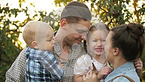 Happy father embracing his family in a Park on a Sunny day. Mom, dad and the little kids laughing and hugging at sunset