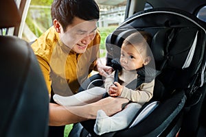 happy father is fastening safety belt to infant baby in car seat