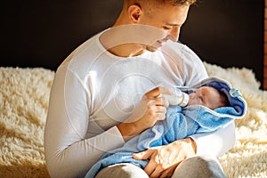 Happy father feeding his newborn son with milk in bed at home