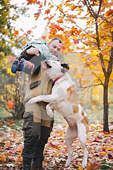 Happy father have fun and lift up their daughter in autumn park next to jumping dog during walk