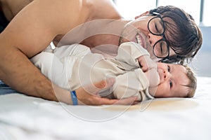 Happy father having fun with his adorable baby boy while playing together over bed. Happy family concept.