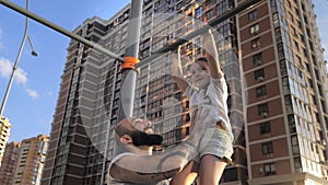 Happy father and his 5-year old daughter do exercises on the crossbar in the city park.Father helps her catching up on