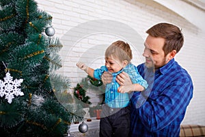 Happy father and his little son decorating the Christmas tree at home.