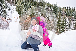 Happy father and his two daughters building a snowman on winter day. Family playing on nature with forest in background.