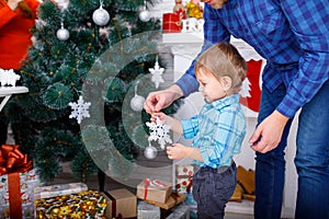 A happy father and his young son decorate the Christmas tree with white snowflakes.